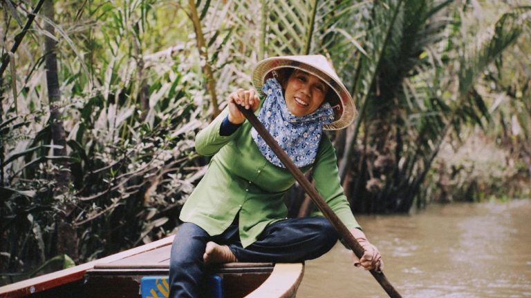 A traveler paddling a wooden boat through dense mangrove forest in the Mekong Delta.