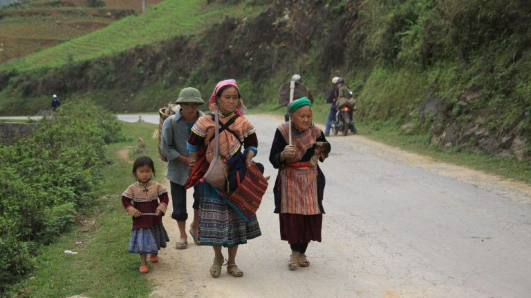 Local villagers walking on a rural mountain road while cyclists pass on a Vietnam cycling tour.