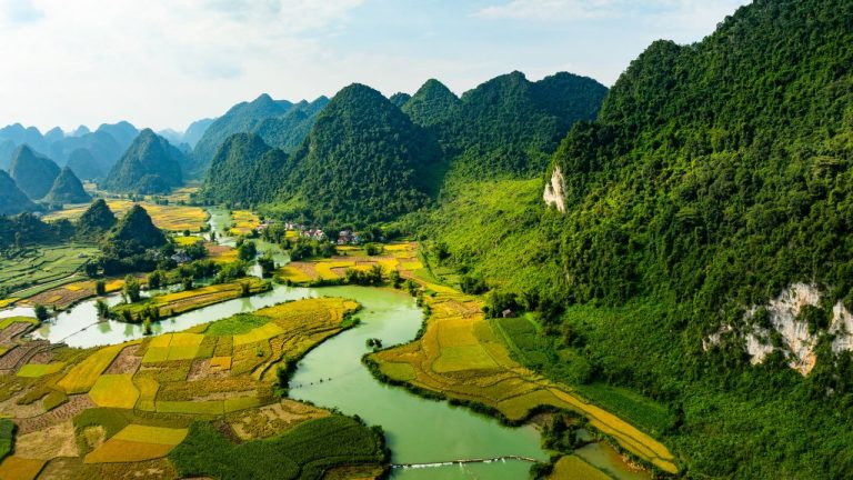 Aerial view of verdant karst mountains, rice paddies, and winding river in northern Vietnam valley.