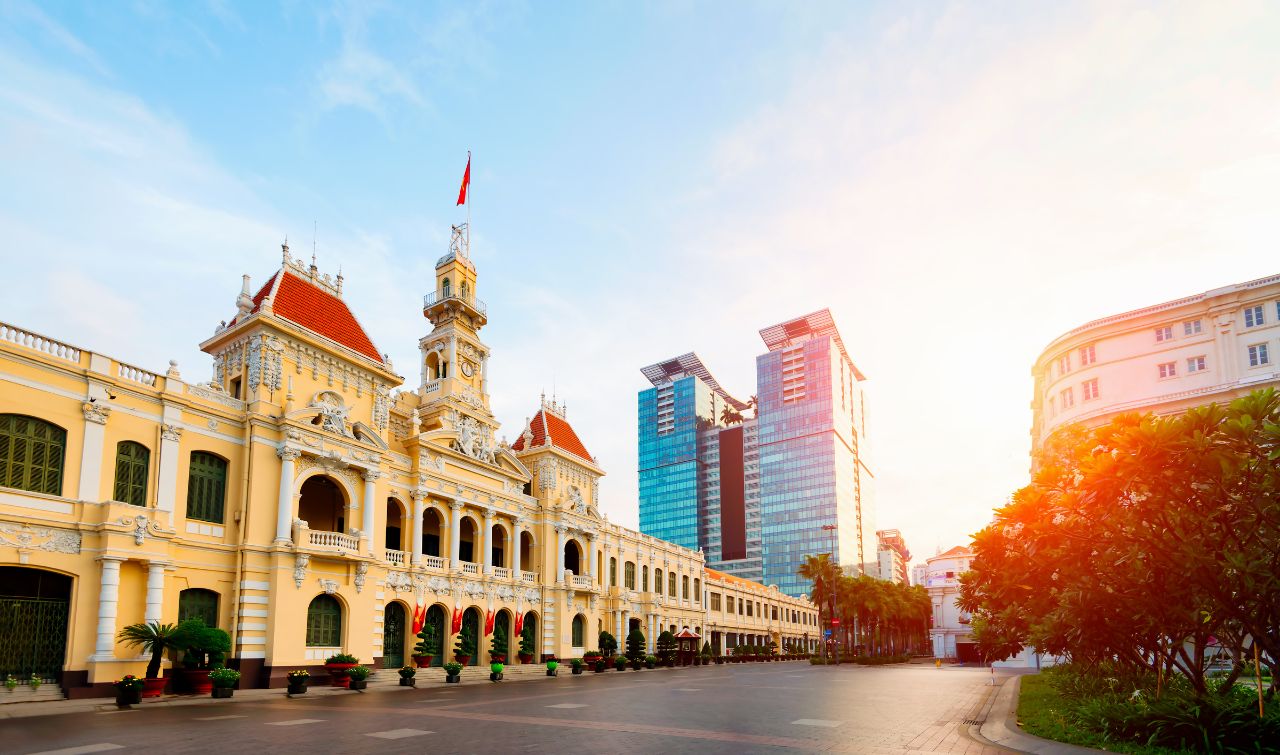 Colonial yellow building with clock tower and red flag in Ho Chi Minh City at sunrise.