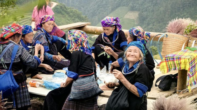 Local villagers wearing traditional colorful headwraps sharing a meal together on a mountainside.