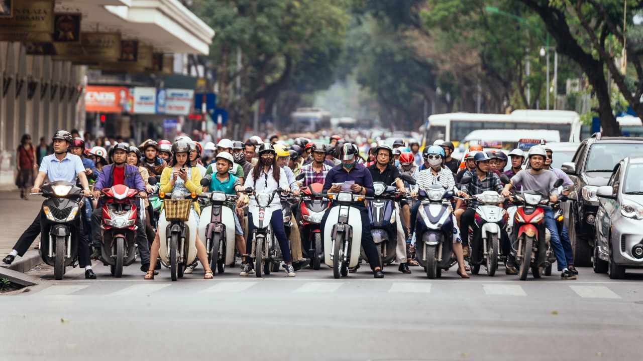 Large group of motorbike riders wearing helmets lined up across a city street.