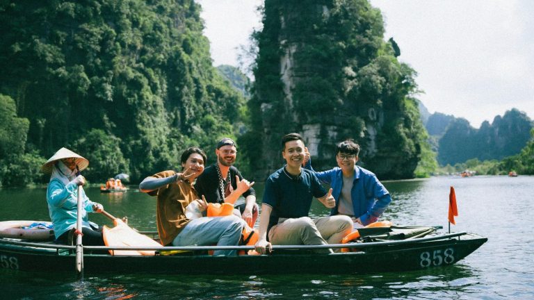 Travelers in a wooden boat on a river surrounded by towering limestone cliffs in Ninh Binh, Vietnam.