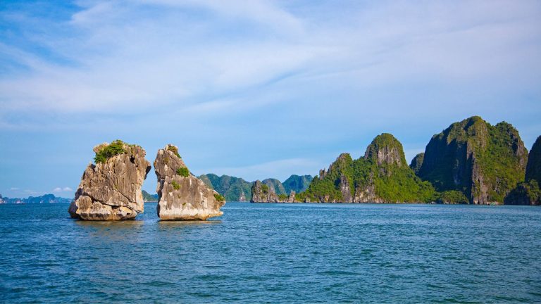 Towering limestone karsts with vegetation rise from turquoise waters under blue sky in Halong Bay.