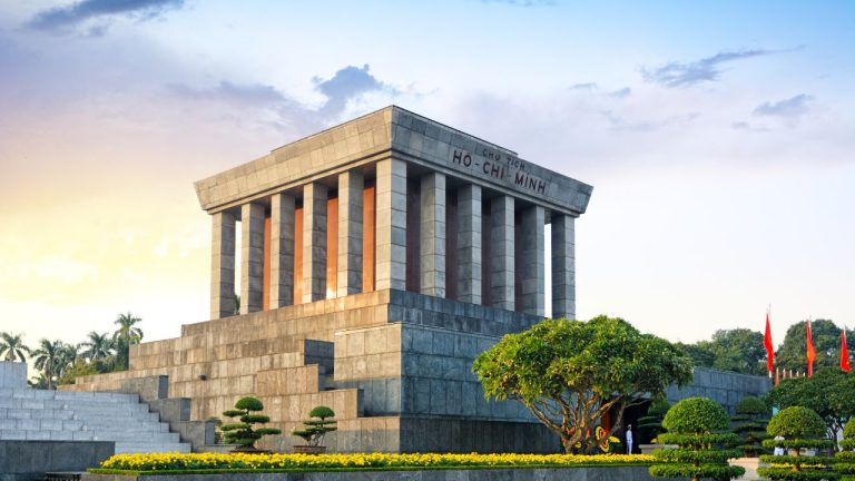 Ho Chi Minh Mausoleum with columned structure, manicured gardens, and red flags in Hanoi.