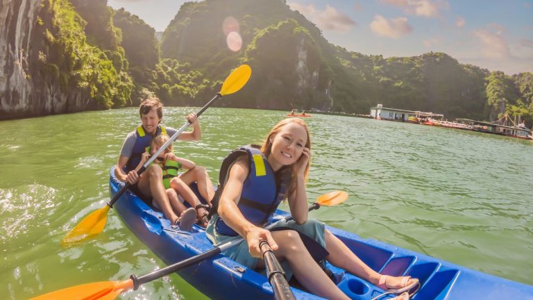 Travelers kayaking in emerald waters surrounded by towering limestone cliffs in Halong Bay.