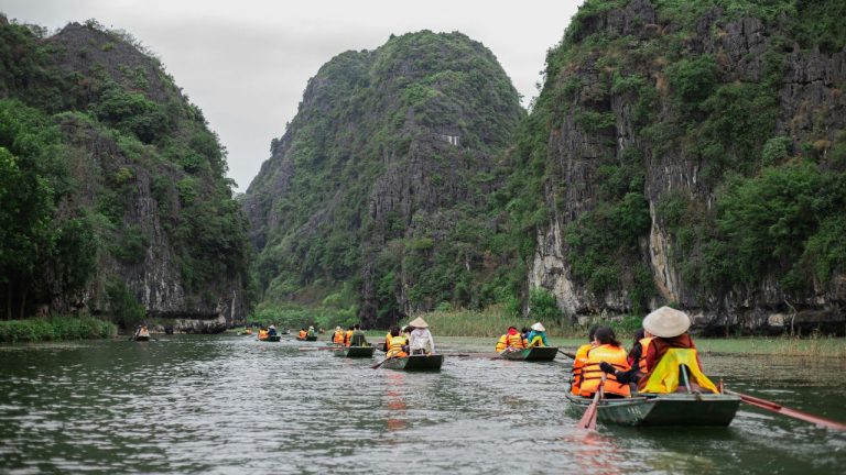 Travelers kayaking between towering limestone karsts in a scenic lagoon surrounded by lush green vegetation.