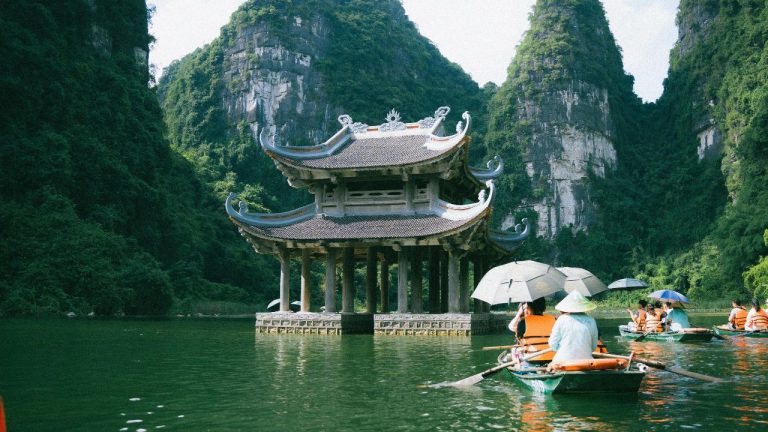 Travelers kayaking past a traditional pagoda with upturned eaves among limestone cliffs in Ninh Binh.