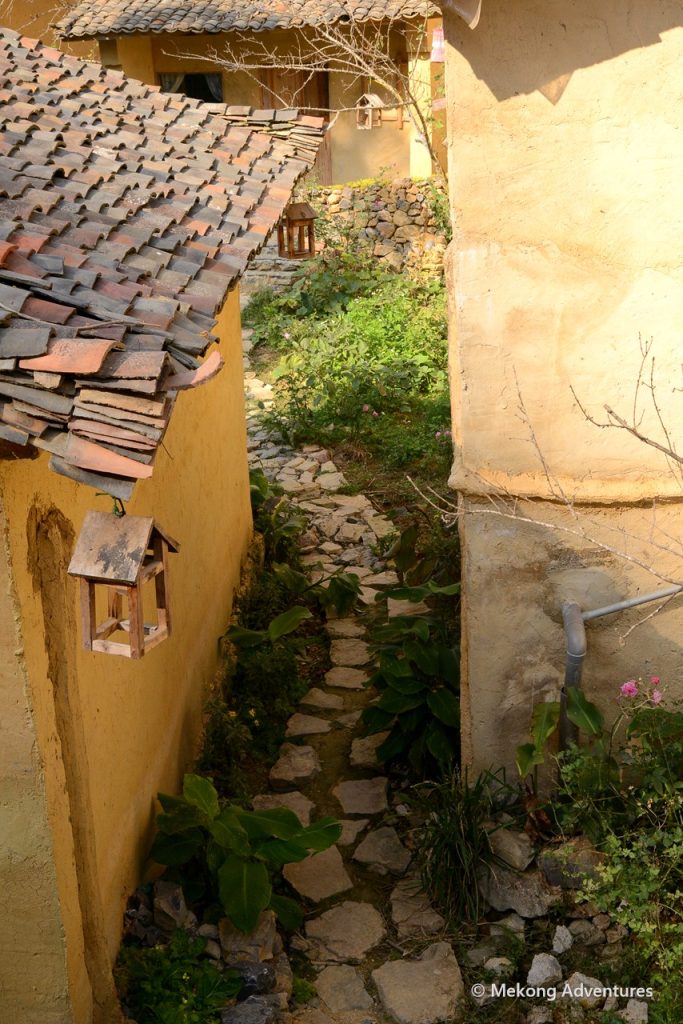 Narrow stone path between earthen houses in Then Pa village